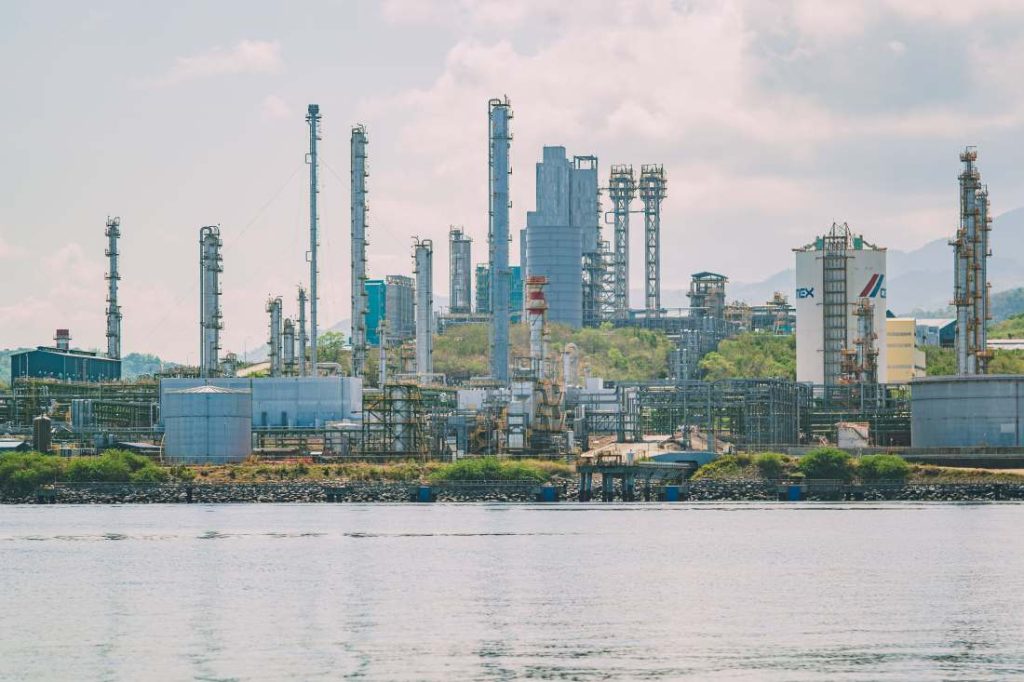 Industrial refinery complex by the shoreline under a cloudy sky.