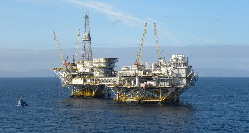 Offshore oil rig platform with cranes in the ocean under a clear sky.
