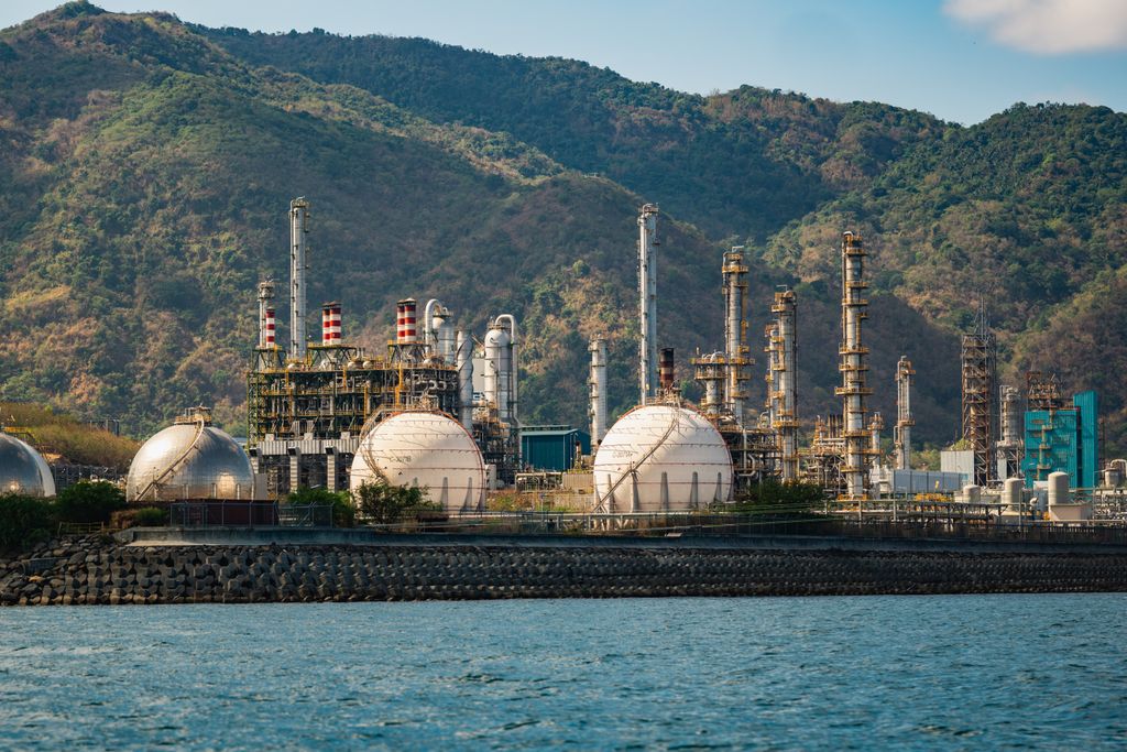 Industrial plant with large tanks near mountains and water.