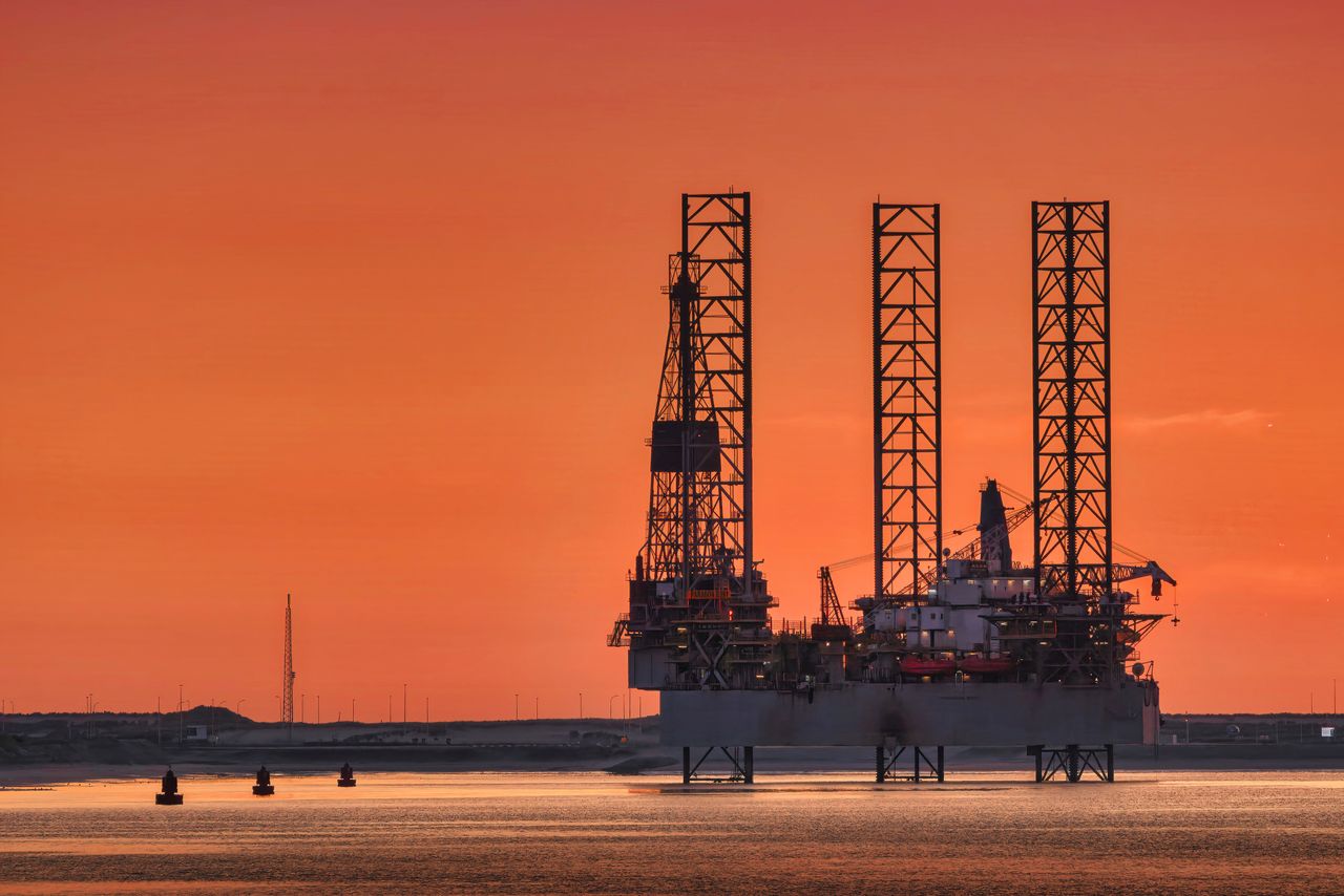 Oil rig silhouette against an orange sunset background