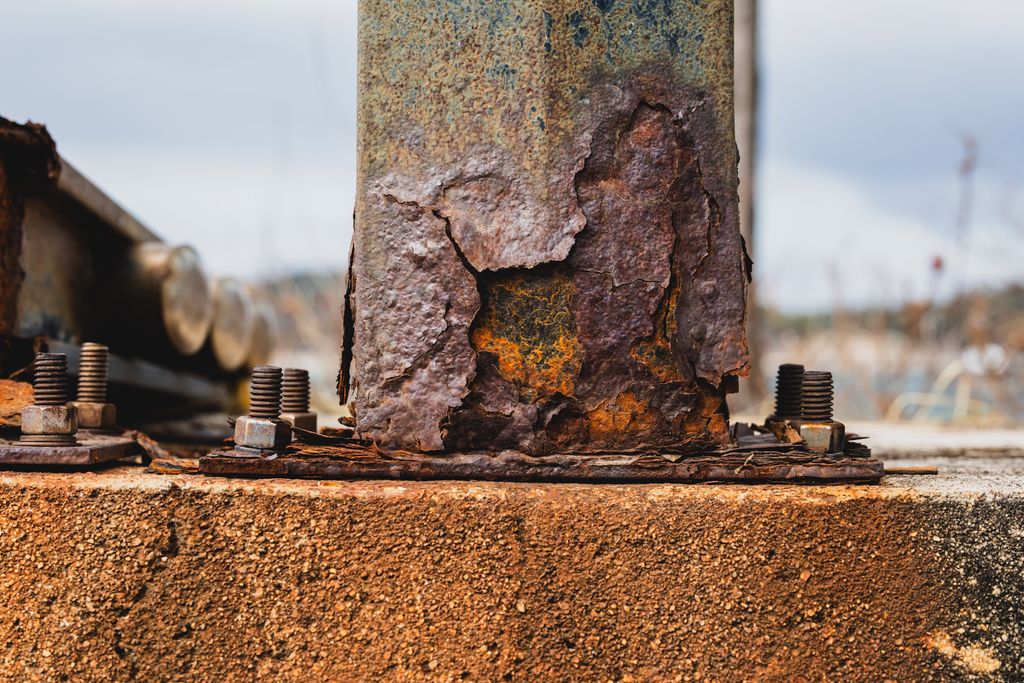 Close-up of rusted metal post with bolts on concrete surface.