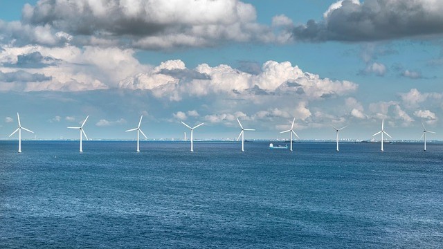 Offshore wind turbines under a cloudy sky over the ocean.