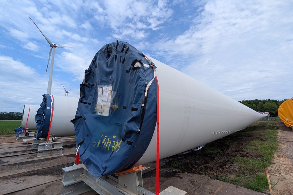 Wind turbine blades stored horizontally with turbines in background.