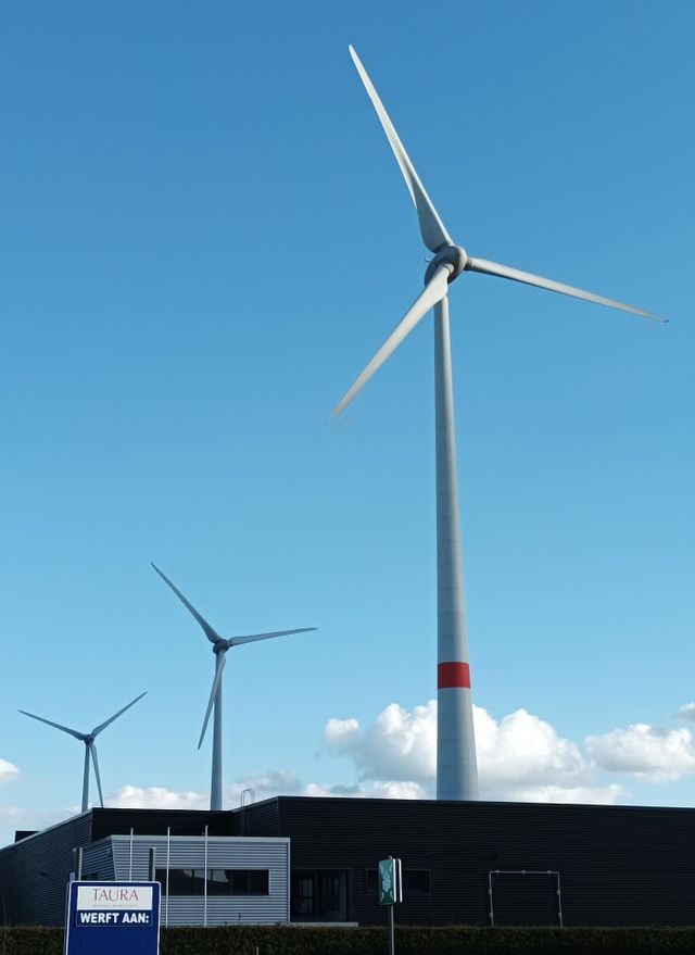 Three wind turbines beside a building under a clear blue sky.